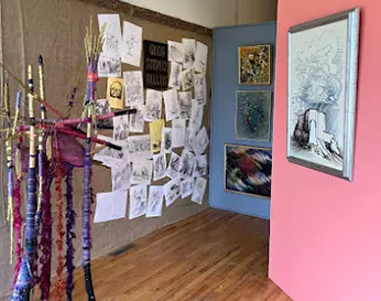 Art on display including yarn sculpture, sketches, and painting hung on pink wall