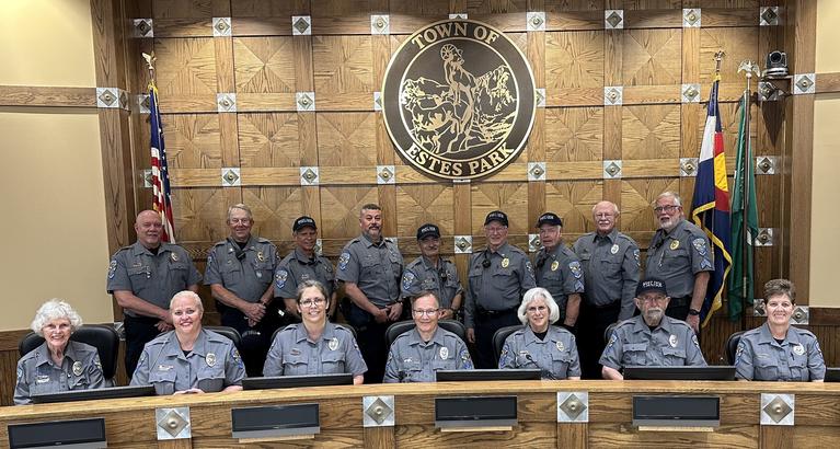 Estes Park Police Auxiliary unit sitting and standing in front of Town of Estes Park seal in board room