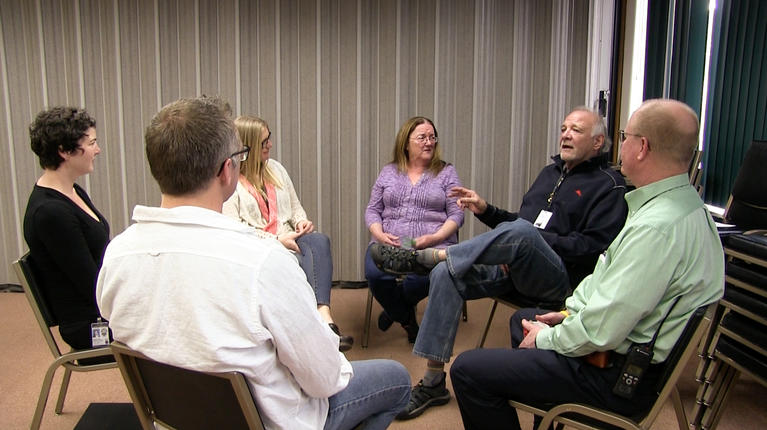 Six people seated in chairs in a circle engaging in conversation